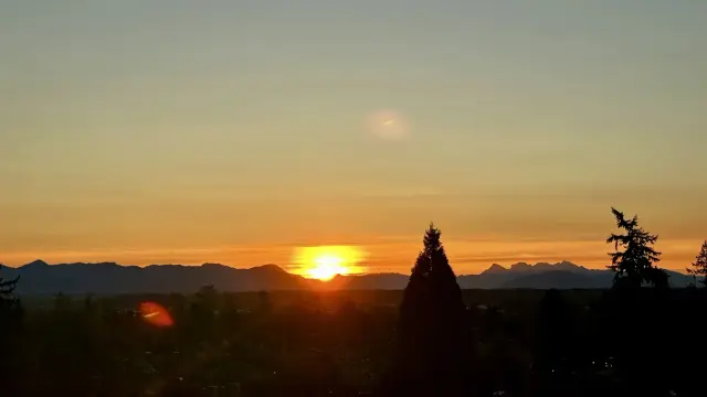 The sun just coming over distant mountains with cirrus illuminated with an orange hue, fading to light blue with altitude.