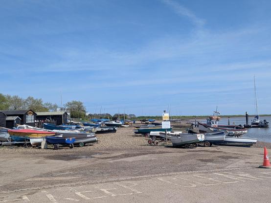 A photo of Orford quay showing the river Alde on the right and the various small boats and dinghy's on the beach. To the left are small fishing huts and a tearoom. A bright blue sky with gentle wisps of alto clouds 
All very peaceful and pleasant.