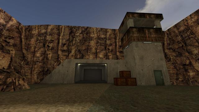 In this picture you can see an entrance that goes into a mountain. In this entrance, two white-lit lamps are mounted on the ceiling. In addition, you can see a roller door further behind in the entrance, which is closed. To the right of the entrance are three dark brown wooden boxes. Two stand on the ground and the third stands on top of the other two in the middle. Next to it is a watchtower. This one had a blue door. Furthermore, there are lamps under the lookout, but they are off. This is on the map cs_siege in the game Counter-Strike 1.6.