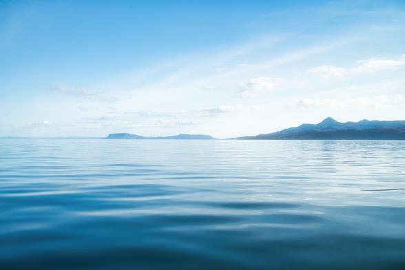 An image of a calm sea with silhouettes of islands on the horizon. Scotland