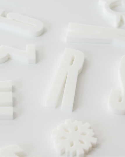 Closeup of white Alphabet Magnets, in the form of the Rainer typeface
