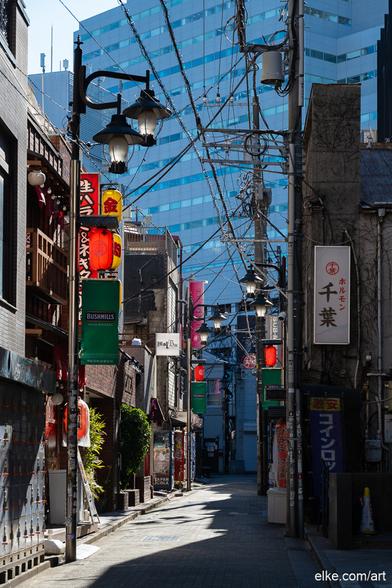 A narrow street in Shibuya, Tokyo, basking in crisp morning light.

Bright red lanterns and Japanese signage line the facades of izakayas and bars, while power cables and vintage streetlamps weave a chaotic web overhead. In the background, a modern office building adds contrast to the dense textures of this traditional alley.

This photograph captures the layered charm of Shibuya, where old meets new in an ever-changing urban rhythm.

Perfect for modern interiors, creative studios, or gallery walls with a passion for global street culture.

Ideal for collectors of Japanese urban photography, Tokyo alleys, or atmospheric street scenes from East Asia.
