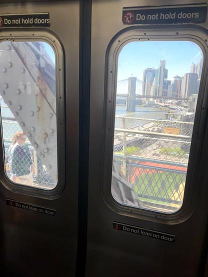 NYC Q train to Brooklyn, view of another bridge, through two subway doors. A beam on our bridge is seen, and a pedestrian on the bridge.