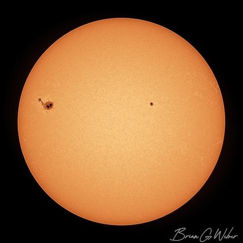 A large cluster of sunspots dominates the left side of the image while a single sunspot on the right side is the only other one really visible.