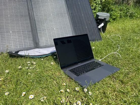 Photo of a solar panel and a laptop on a green meadow.