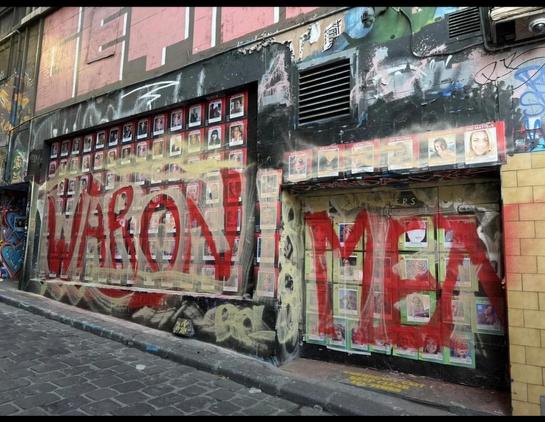 The She Matters mural, with the faces of women killed by male violence. It has been painted over with red paint in huge letters, saying "War On Men"