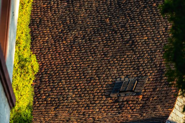 Kleines altes Dachfenster aus Metall mit Kreuzsprosse. Umrandet mit Schindeln aus Schiefer in einer Dachfläche aus handgestrichenen Biberschwanzziegeln.