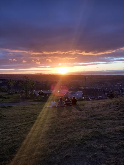 Four people sit on a hill watching the sunset