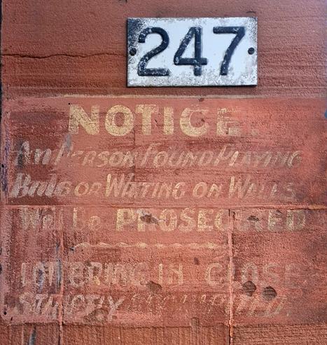 A ghost sign painted on a red sandstone tenement wall which reads Notice. Any person found playing balls or writing on walls will be prosecuted  loitering in close strictly prohibited.