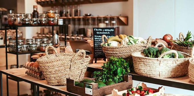 Photo of products on display inside an eco-market, with fruits and vegetables in woven baskets, and with other items in glass jars rather than plastic.