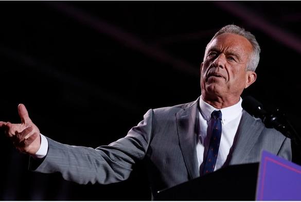 Photo of Robert F Kennedy Jr speaking at a podium with a dark background. He is reaching with his right hand off to the side. [Photo credit: the Washington Post]