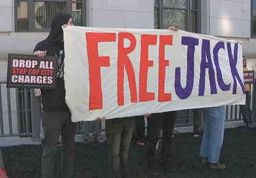People hold up a banner reading, "Free Jack" outside of a court house.