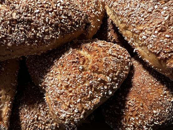 Auf einem dunklen Holztisch liegt ein Holzbrett. Darauf liegen zahlreiche frisch gebackene Brötchen mit rustikalem Ausbund