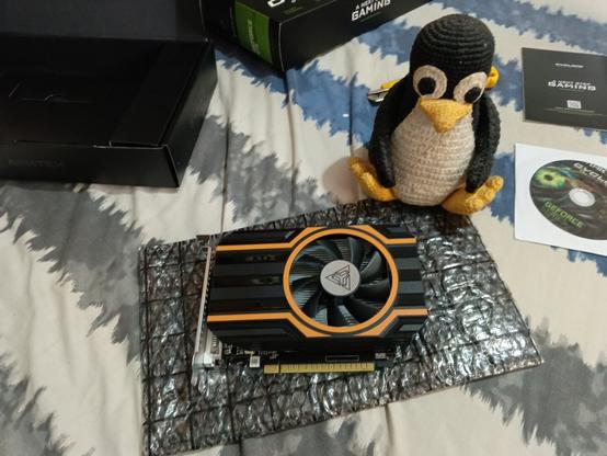 A photo of a GPU atop an antistatic bag, near an embroidered Tux plushie and with the contents of the GPU box strewn about.