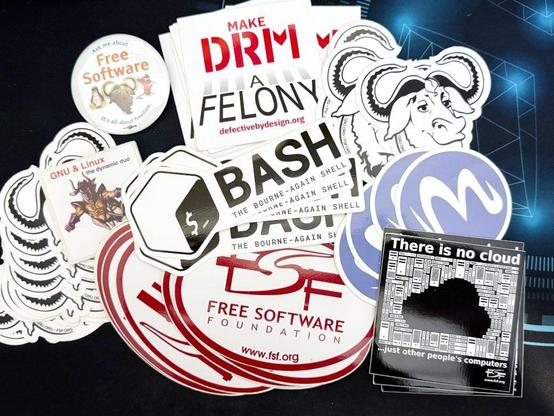 Foto de surtido de pegatinas de temas de software libre: bash, free software foundation, logo de emacs, cabeca de GNU, DRM a Felony y There is no cloud