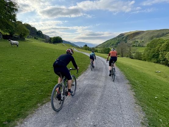 three cyclists riding on a gravel track down a grassy valley