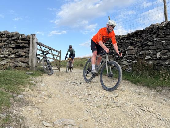 two cyclists riding through 5 bar gate on a gravel track