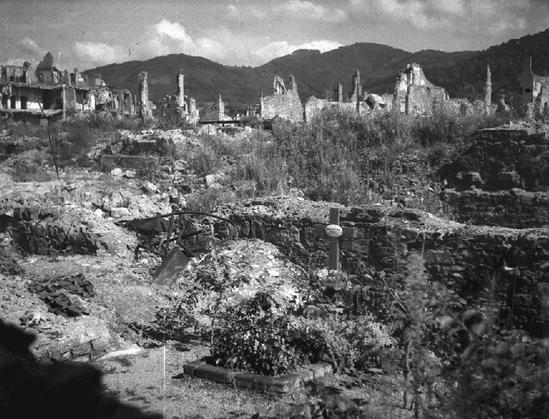 Kriegsschäden in Freiburg im Jahr 1945. Im Vordergrund ein Grab, im Hintergrund zerstörte Gebäude.