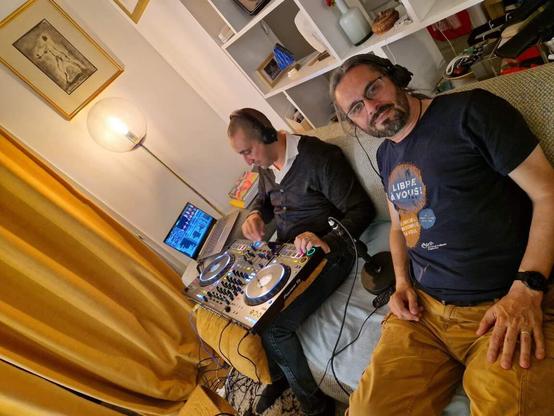 Sur un canapé : Mehdi avec une console Pionner DJ sur les genoux, son ordinateur avec Serato DJ. Fred à côté juste avant un casque devant la console RodeCASTER qu'on ne voit pas sur l'image.