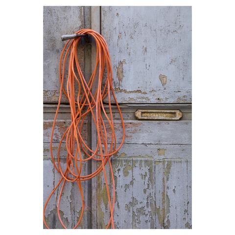 Flat closeup of a weathered, light blue wooden door. The blue paint has come off on parts of the door. A small mail slot sits in the center. An orange electrical cable has been wrapped multiple times around the door handle.