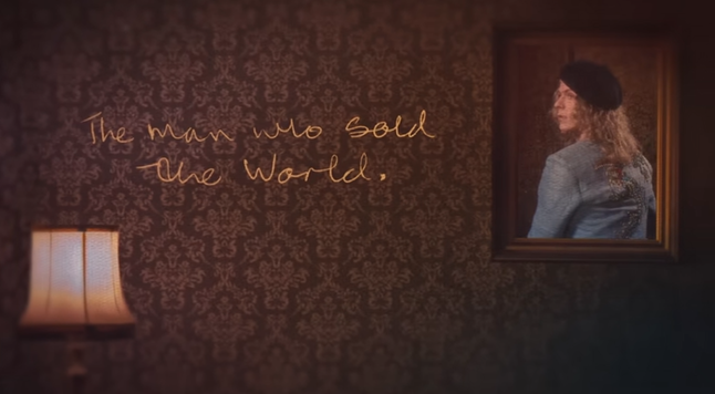 David Bowie's picture profile on the righthand top in a portrait wooden frame shot from the back wearing a light blue vest and a black beret, with the title written in gold on a brown background next to it, and pink lampshade on the lefthand bottom.