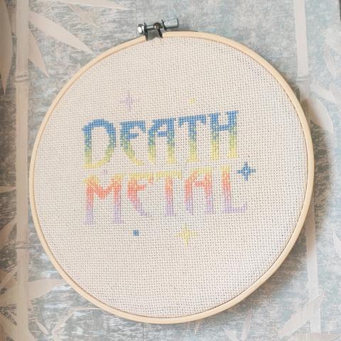 Off white aida in a finished 20cm hoop.

The text is a large font and reads "death metal", there are also a few stars scattered around it.

The work is blue on top, goes into green, yellow, orange and finally purple. All the colours are pastels or close to pastels.