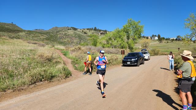 A man in a blue FCRC (Fort Collins Running Club) tank top and a bib with number 382 descending a dirt trail.