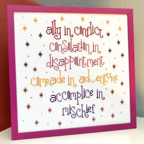 Cross-stitch in a square fuschia frame reading "ally in conflict, consolation in disappointment, comrade in adventure and accomplice in mischief." 

Each section of the phase is stitched in ombre of red, pink, orange and purple. There are randomly placed stars stitched in the opposite of the ombre that fill in the rest of the white background.