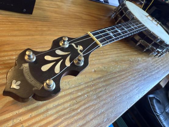 A shot down the neck of a banjo lying on a wooden desk, the drum in the background on the upper right.