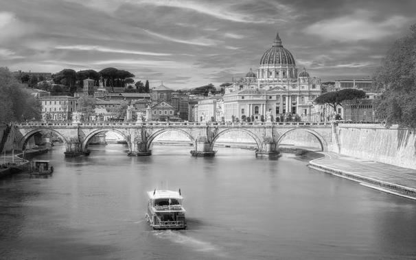 A black and white image of a view of Vatican City. A boat in the Tiber River is in the foreground with the Ponte Sant'Angelo in the midground. In the distance rises the dome of St Peter's Basilica of Vatican city.