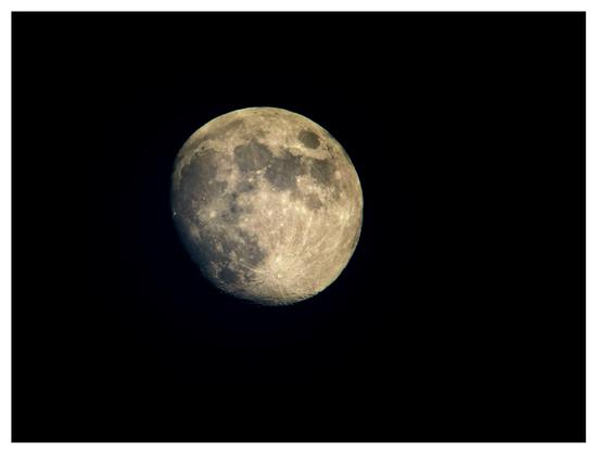 A waxing gibbous moon, nearly full, against a black background. The moon has a warm tone and its surface details are visible. The image is framed by a white border.