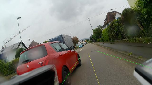 Sicht eines Radfahrers, ein roter PKW überholt extrem nah. Es sind Linien eingezeichnet, die 1m Abstand visualisieren sollen, diese sind aber wegen des vermutlich falschen Kamerawinkels offensichtlich nicht korrekt.