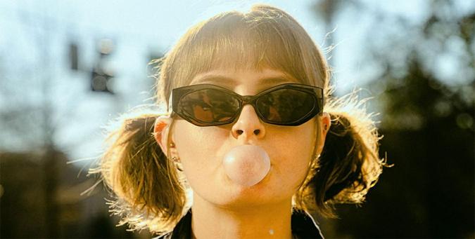 A woman wearing sunglasses and pigtails blows a gum bubble facing the camera A woman wearing sunglasses and pigtails blows a gum bubble facing the camera