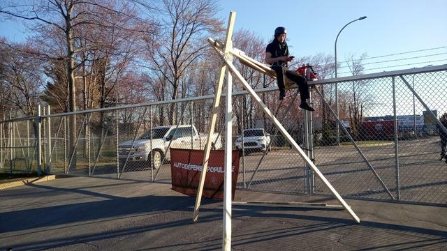 Un homme est assis sur une structure de bois devant des portes grillagées.