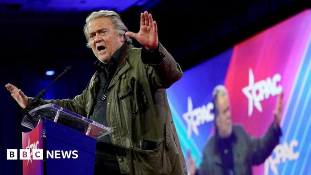 Steve Bannon in the midst of a speech in front of a large illuminated screen, waving his arms