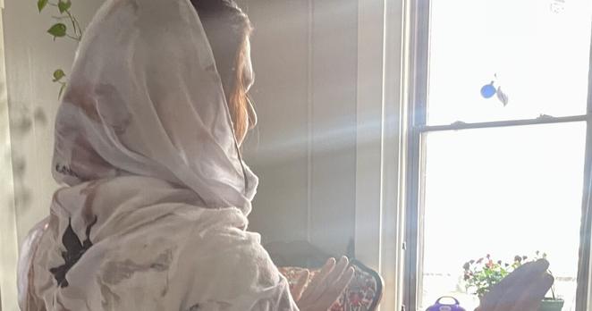 Woman facing away from camera holding her hands up towards a sunlit window