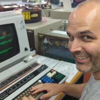 Photo of me, a white man with a short dark beard, and dark hair, smiling at the camera, while sitting in front of a vintage terminal with green text on the screen. Photo of me, a white man with a short dark beard, and dark hair, smiling at the camera, while sitting in front of a vintage terminal with green text on the screen.