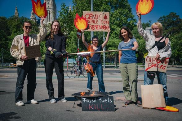 5 Personen stehen vor dem Rathaus. Am Boden ist eine Feuerschale und zwei der Personen halten darüber einen Spieß, auf dem Fake-Geldscheine montiert sind - wie zum Grillen.
Die Person in der Mitte hält ein Demoschild mit der Aufschrift "Genug Kohle zum verbrennen.".