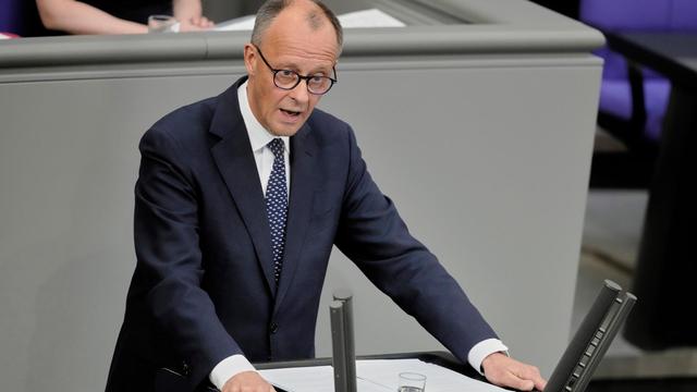Das Foto zeigt Friedrich Merz am Rednerpult des Bundestags. Er trägt dunkelblauen Anzug und eine blaue Krawatte. Seine Arme stützt er auf das Pult. Das Foto zeigt Friedrich Merz am Rednerpult des Bundestags. Er trägt dunkelblauen Anzug und eine blaue Krawatte. Seine Arme stützt er auf das Pult.