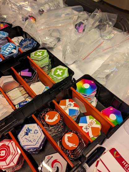 a box full of different stickers from project that NLNET has funded. including the green mapcomplete icon with the white plus in the green circle/pin.