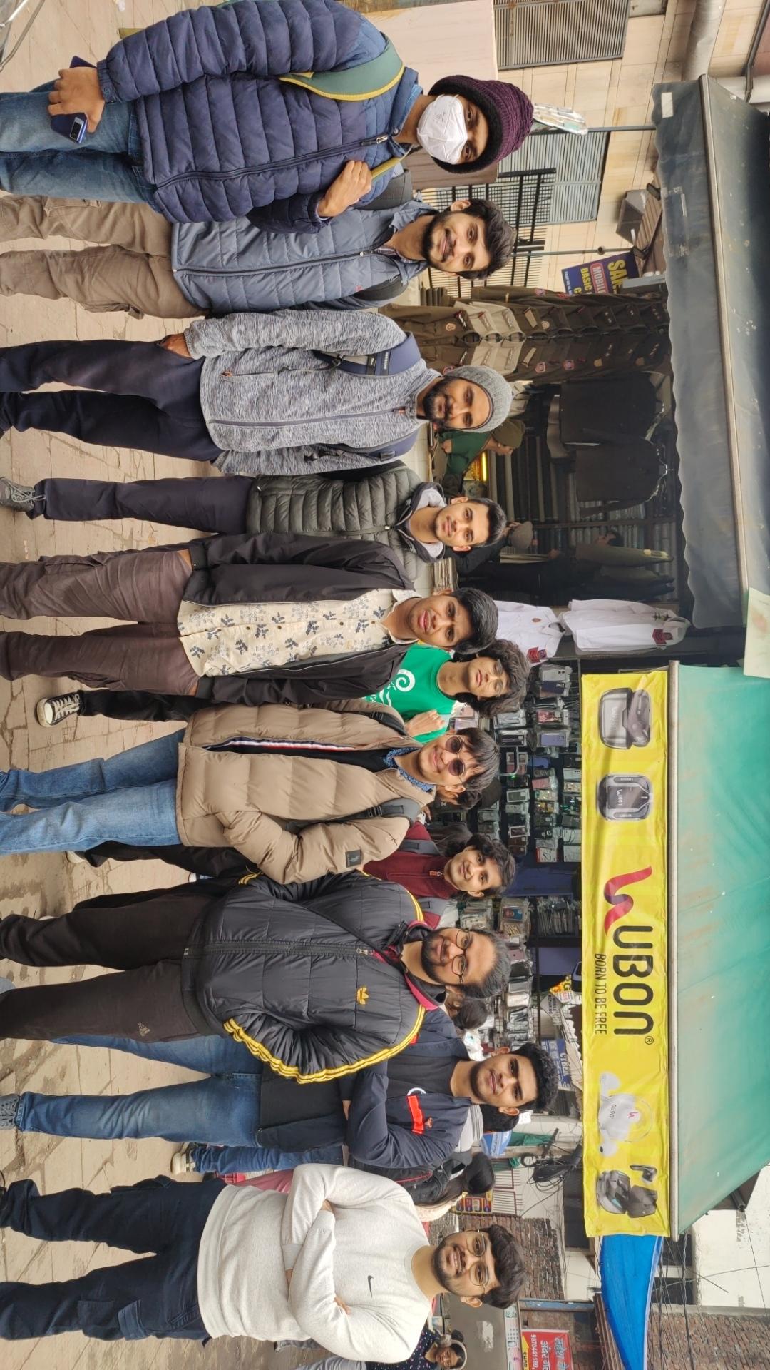 11 young men standing on a sidewalk in front of some shops, smiling at the camera.