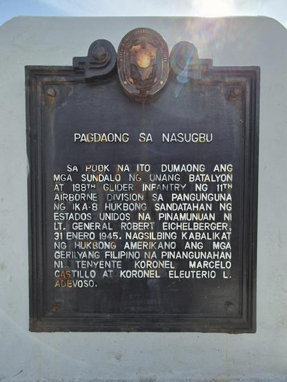 Cast iron historical marker with the following white text on black:

Pagdaong sa Nasugbu
Sa pook na ito dumaong ang mga sundalo ng Unang Batalyon at 188th Glider Infantry ng 11th Airborne Division sa pangunguna ni Lt. General Robert Eichelberger, 31 Enero 1945. Nagsilbing kabalikat ng hukbong Amerikano ang mga gerilyang Filipino na pinangunahan ni Tenyente Koronel Marcelo Castillo at Koronel Eleuterio L. Adevoso.