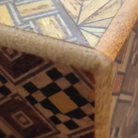 Macro shot of a corner of a wooden box. The sides of the box are covered in a Japanese yosegi pattern consisting of geometric shapes of different colors of wood.