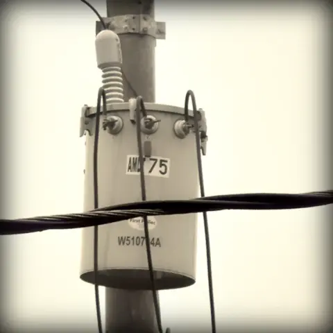 Sepia-toned photo of a residential electrical transformer mounted on a pole an with a thick electrical wire passing in front of it