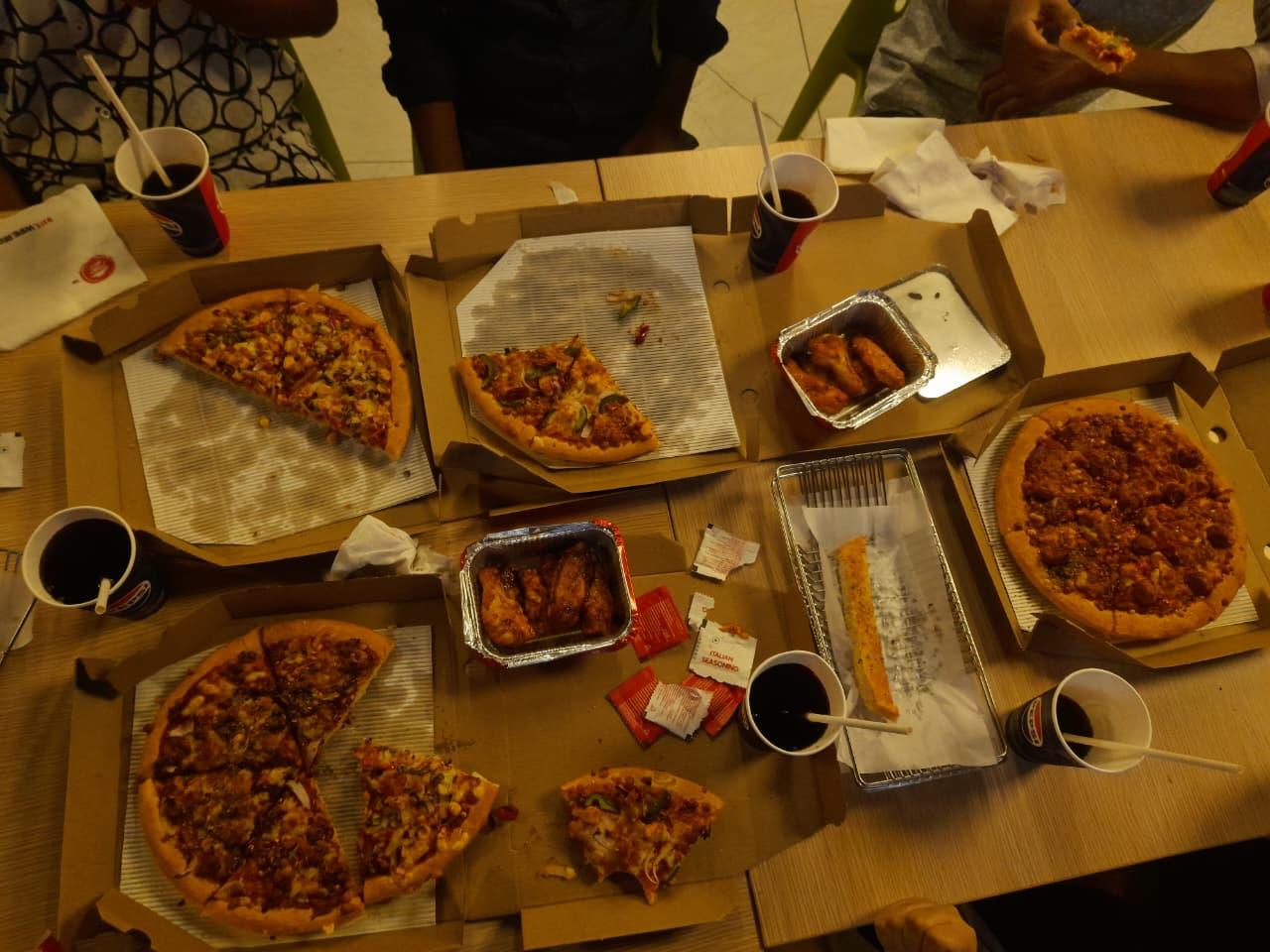 A view of the food ordered after the mapping party from above. 4 medium-sized pizzas, some of them eaten halfway while taking the picture, along with baskets of garlic bread, a couple of portion of chicken wings and cups of soda.