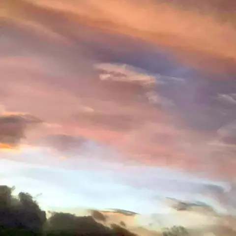 Stratus clouds at sunset in various shades of orange-gray with some silhouetted cumulus clouds in the lower foreground