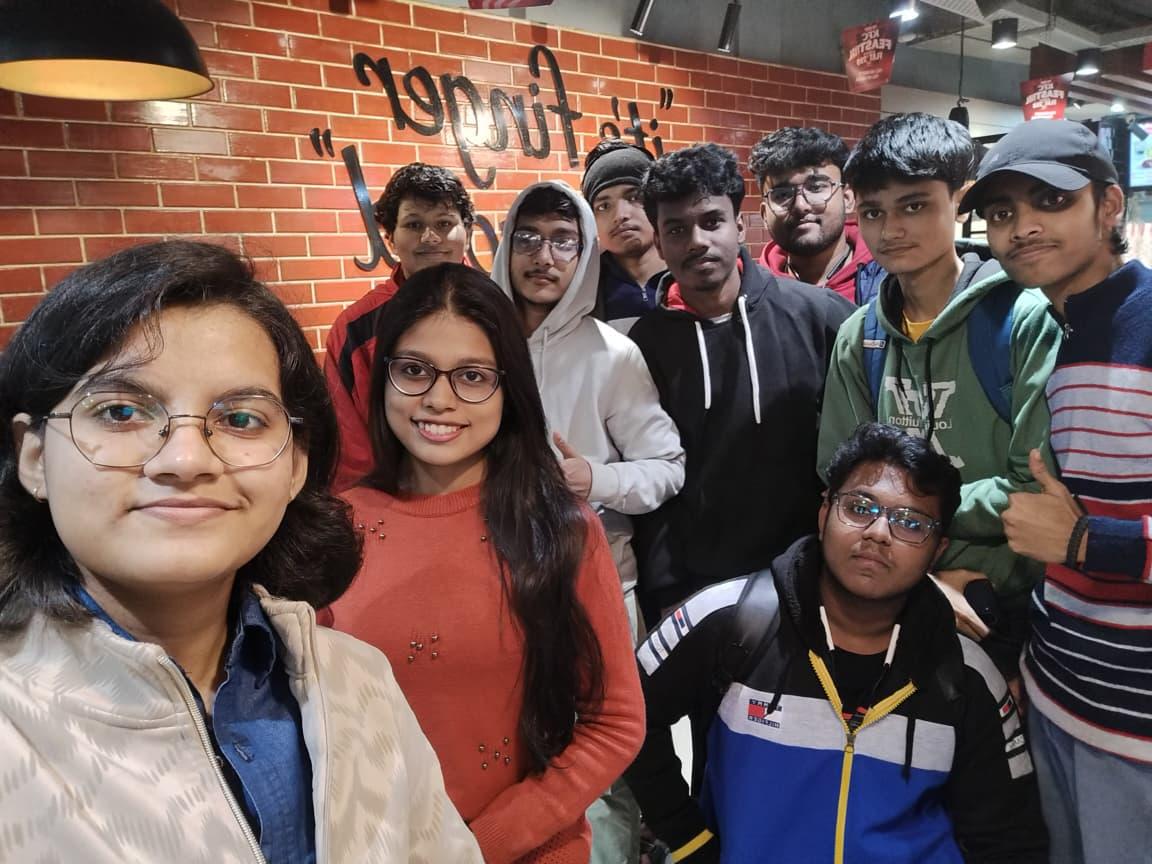 A group of 10 people, 2 women and 8 men, looking at the camera. The person on the right, and the fourth person from the left in a white hoodie, raising their thumbs up.