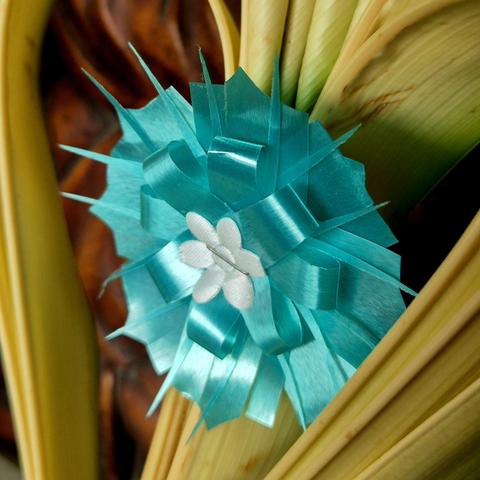 Turquoise-colored floral piece made out of plastic ribbon set at the middle of a folded palm frond