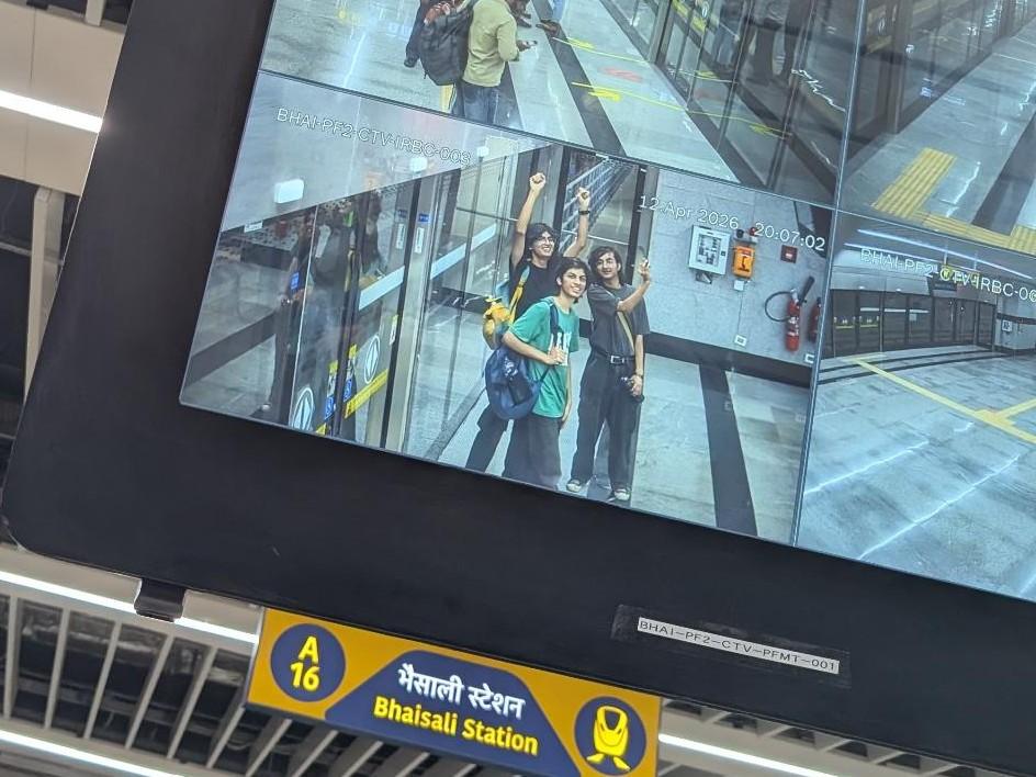 Photo of an electronic display at Bhainsali Metro station, Meerut. 

The display is showing four surveillance camera feeds. The photo is centered on the bottom-left feed, which shows three people happily posing into a surveillance camera. One of them is holding up a phone to their left, without looking at it - that, you realize, is how this photo was taken.

In the background visible below the display, a yellow-and-blue sign says "A16 Bhaisali Station".