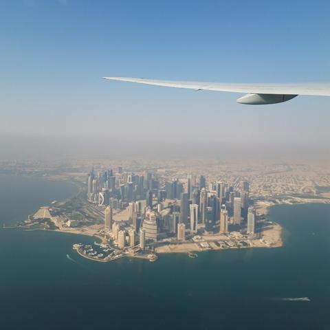 View out of an airplane window overlooking a slightly hazy peninsula filled with skyscrapers, desert in the background towards the horizon, and part of the left wing visible